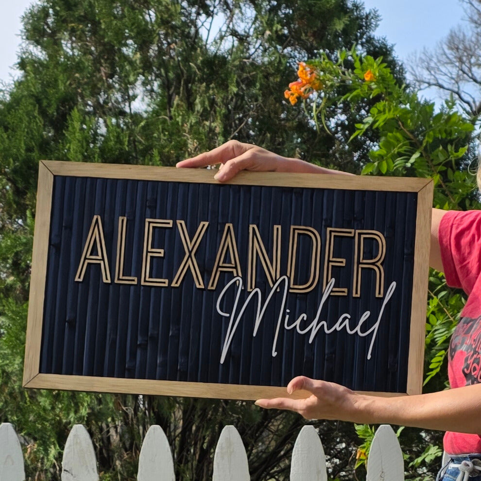 Person holding a framed name sign with 'Alexander Michael' outdoors.